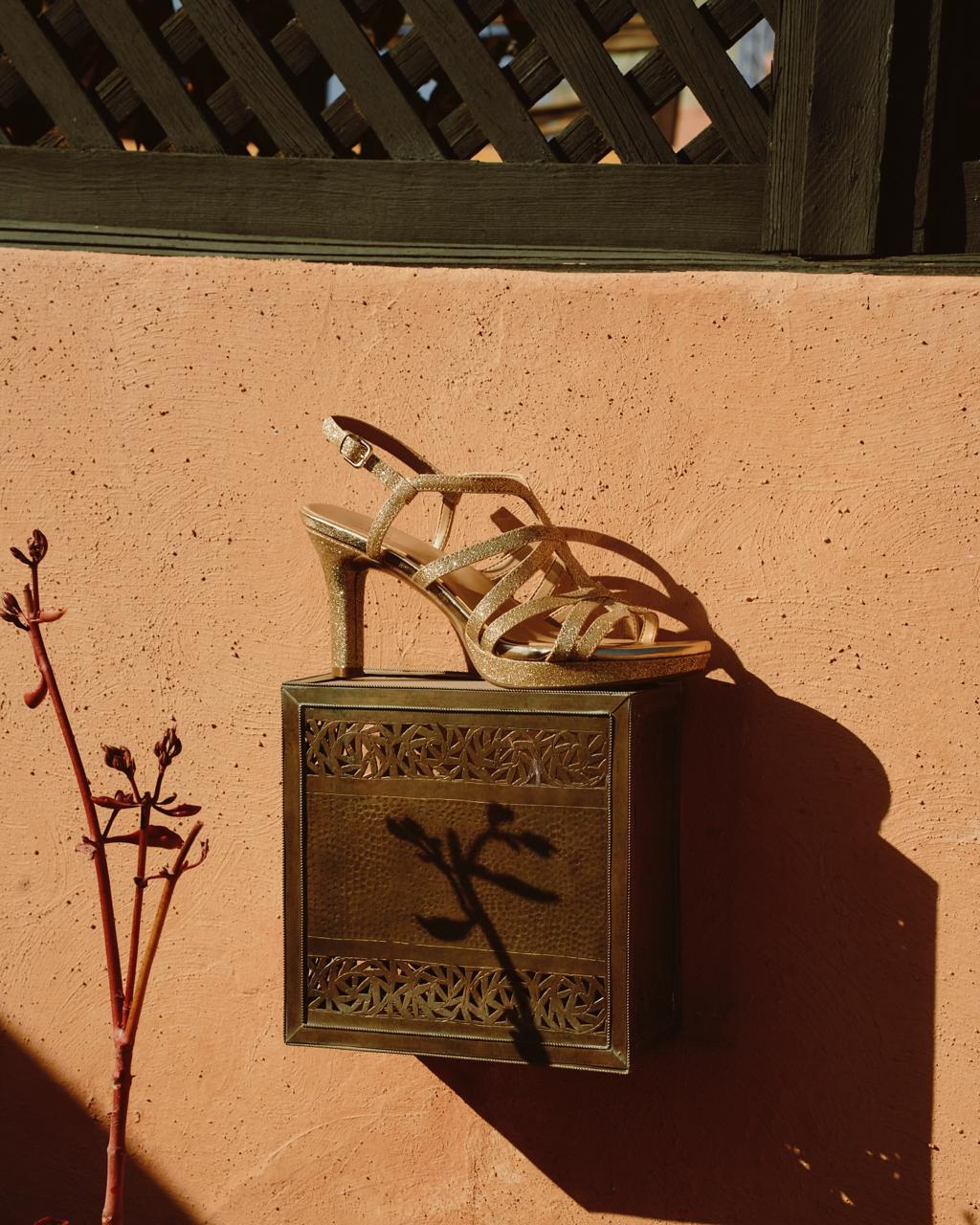 Gold glitter strap sandal on a brass wall box