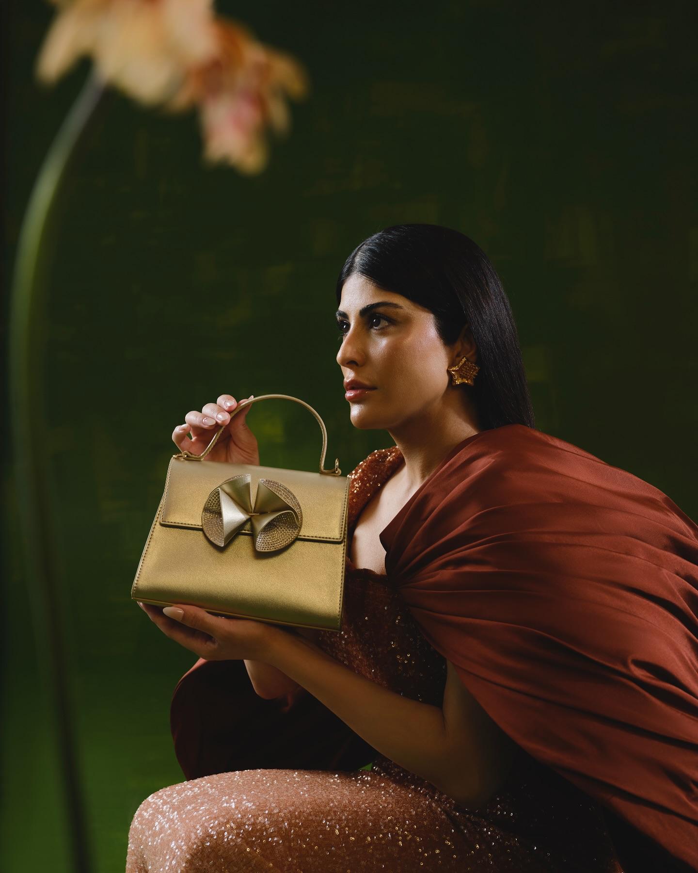 Zaara Al Balushi holding a gold Nine West bag against a deep green backdrop